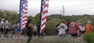A group of runs pass by two American flag post during the Forever Brave marathon.